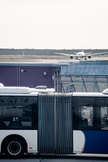 View of an airport shuttle bus parked on the tarmac with an airplane taxiing on the runway in the background at Frankfurt Airport in Frankfurt am Main Hessen Germany.