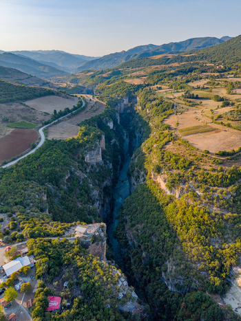 Aerial view of Osumi Canyon featuring a deep river gorge with steep limestone cliffs lush green vegetation and a winding road in the surrounding landscape of Dhores Berat County Albania.