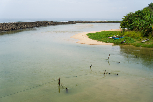 View of a coastal lagoon with traditional wooden boats on the sandy shore and a stone breakwater in Koggala Southern Province Sri Lanka. View of a coastal lagoon with traditional wooden boats on the sandy shore and a stone breakwater in Koggala Southern Province Sri Lanka.