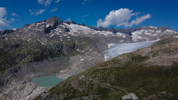 Aerial view of Furka Pass and the Rhone Glacier featuring rugged mountain peaks a turquoise glacial lake and winding alpine roads in Obergoms Valais Switzerland. Aerial view of Furka Pass and the Rhone Glacier featuring rugged mountain peaks a turquoise glacial lake and winding alpine roads in Obergoms Valais Switzerland.