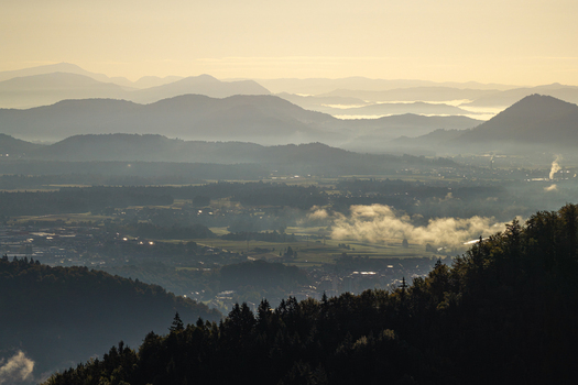 Aerial view of the misty valley and rolling mountains at sunrise with dense forests and soft morning light in Kranj Slovenia.