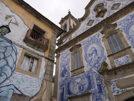 View of the Church of Santa Maria Maior with its ornate blue and white azulejo tile facade standing beside an old building adorned with modern graffiti in Covilha Castelo Branco Portugal. View of the Church of Santa Maria Maior with its ornate blue and white azulejo tile facade standing beside an old building adorned with modern graffiti in Covilha Castelo Branco Portugal.
