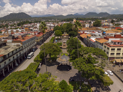 Aerial view of the main square in Centro featuring a central gazebo lush trees colonial architecture and distant mountains in Uruapan Michoacan Mexico.