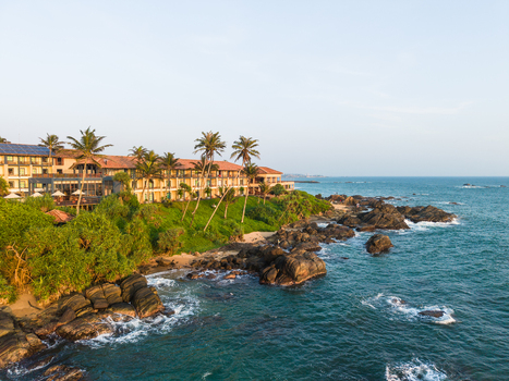 Aerial view of a luxury coastal resort nestled among palm trees and greenery on a rocky shoreline overlooking the turquoise Indian Ocean in Galle Southern Province Sri Lanka. Aerial view of a luxury coastal resort nestled among palm trees and greenery on a rocky shoreline overlooking the turquoise Indian Ocean in Galle Southern Province Sri Lanka.
