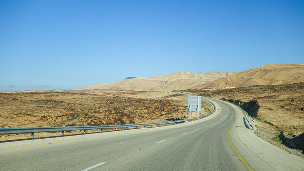 View of a paved road winding through the arid desert landscape of Wadi Musa with rocky hills under a clear blue sky in Wadi Musa Ma an Governorate Jordan. View of a paved road winding through the arid desert landscape of Wadi Musa with rocky hills under a clear blue sky in Wadi Musa Ma an Governorate Jordan.