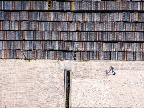 Aerial view of a worker raking crops on a large drying ground with rows of drying noodles on racks in Polanharjo Central Java Indonesia.