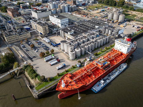 Aerial view of a large red tanker ship docked at the industrial port with storage tanks parked tanker trucks and warehouse buildings in Hamburg Germany.