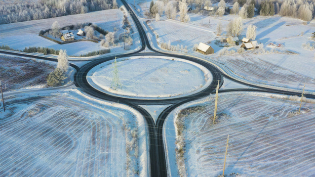 Aerial view of a roundabout surrounded by snow covered fields frost covered trees and rural houses in Latvija. Aerial view of a roundabout surrounded by snow covered fields frost covered trees and rural houses in Latvija.
