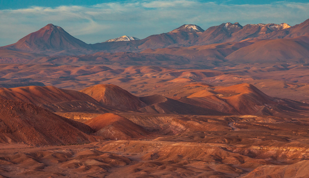Aerial view of the vast Atacama Desert with its rugged rolling red brown hills and distant snow capped mountains under a clear sky in San Pedro de Atacama Antofagasta Chile. Aerial view of the vast Atacama Desert with its rugged rolling red brown hills and distant snow capped mountains under a clear sky in San Pedro de Atacama Antofagasta Chile.
