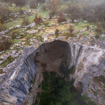 Aerial view of the Prohodna Cave limestone karst formation with its large natural bridge entrance surrounded by rocky terrain and autumn vegetation in Karlukovo Lovech Bulgaria. Aerial view of the Prohodna Cave limestone karst formation with its large natural bridge entrance surrounded by rocky terrain and autumn vegetation in Karlukovo Lovech Bulgaria.