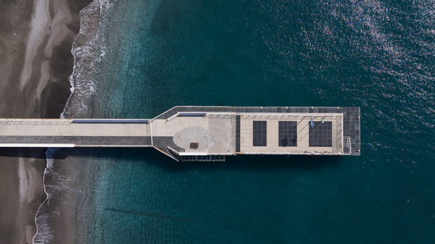 Aerial view of a pier extending into the tranquil deep blue sea where the dark sand meets the foamy waves Minori Salerno Italy Aerial view of a pier extending into the tranquil deep blue sea where the dark sand meets the foamy waves Minori Salerno Italy