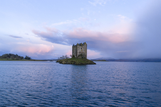 Aerial view of Castle Stalker on a small island surrounded by calm waters under a sunset sky with pink clouds in Appin Scotland United Kingdom. Aerial view of Castle Stalker on a small island surrounded by calm waters under a sunset sky with pink clouds in Appin Scotland United Kingdom.