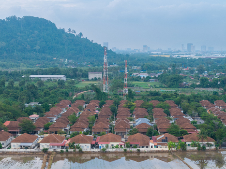 Aerial view of two telecommunication towers rising above a dense residential neighborhood with brown roofed houses and lush green trees in Central Seberang Perai Penang Malaysia.