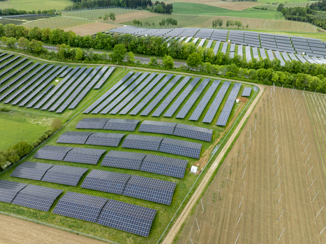 Aerial view of a large solar farm with rows of photovoltaic panels surrounded by green fields and lush trees in Aiglsbach Bavaria Germany.