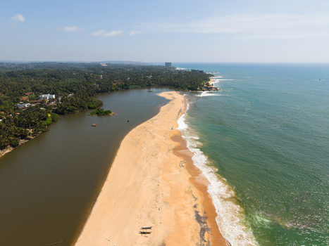 Aerial view of a narrow sandy beach separating a calm lagoon from the turquoise ocean waves under a clear blue sky Galle Southern Province Sri Lanka.