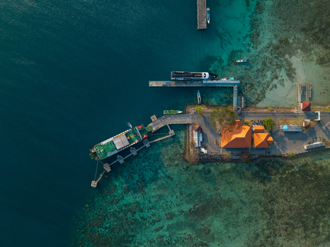 Aerial view of Karimunjawa Port with a ferry docked at the pier surrounded by turquoise coral reef waters and coastal buildings in Karimunjawa Jawa Tengah Indonesia. Aerial view of Karimunjawa Port with a ferry docked at the pier surrounded by turquoise coral reef waters and coastal buildings in Karimunjawa Jawa Tengah Indonesia.