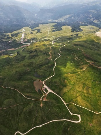 Aerial view of winding mountain roads snaking through lush green alpine meadows and small ponds in the Dolomite Mountains Canazei Trentino South Tyrol Italy. Aerial view of winding mountain roads snaking through lush green alpine meadows and small ponds in the Dolomite Mountains Canazei Trentino South Tyrol Italy.