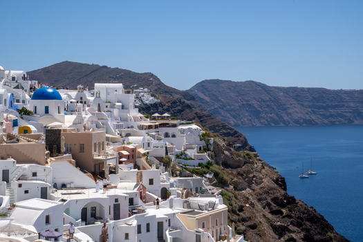 View of white houses and a blue domed church on the cliffs overlooking the Aegean Sea with people on the terraces Fira Greece. View of white houses and a blue domed church on the cliffs overlooking the Aegean Sea with people on the terraces Fira Greece.