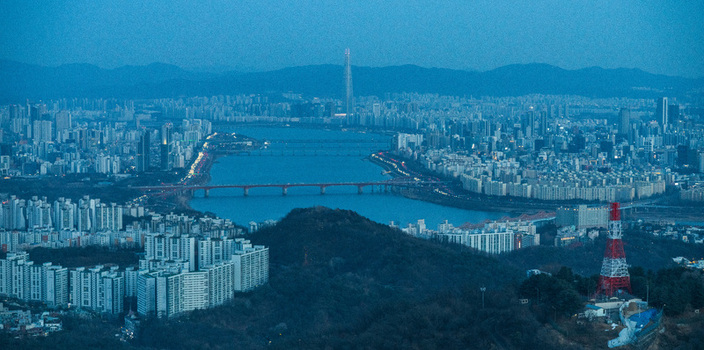 Aerial view of the Han River flowing through the dense urban skyline at dusk featuring high rise apartment complexes bridges and the distant Lotte World Tower in Seoul South Korea. Aerial view of the Han River flowing through the dense urban skyline at dusk featuring high rise apartment complexes bridges and the distant Lotte World Tower in Seoul South Korea.