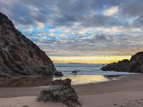 View of a secluded sandy beach nestled between rugged rocky cliffs under a dramatic cloudy sky at sunset in Plettenberg Bay Western Cape South Africa. View of a secluded sandy beach nestled between rugged rocky cliffs under a dramatic cloudy sky at sunset in Plettenberg Bay Western Cape South Africa.