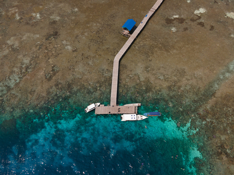 Aerial view of Yenbuba jetty extending into the turquoise waters of the coral reef with boats docked alongside in Raja Ampat Southwest Papua Indonesia. Aerial view of Yenbuba jetty extending into the turquoise waters of the coral reef with boats docked alongside in Raja Ampat Southwest Papua Indonesia.