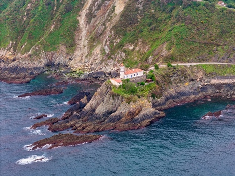 Aerial view of the Faro de Cudillero lighthouse perched on a rocky cliff overlooking the blue Cantabrian Sea with lush green hillsides Cudillero Asturias Spain. Aerial view of the Faro de Cudillero lighthouse perched on a rocky cliff overlooking the blue Cantabrian Sea with lush green hillsides Cudillero Asturias Spain.
