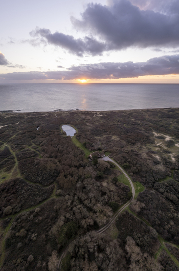 Aerial view of a coastal landscape at sunset with a small pond a house and a winding path leading to the sea in Audresselles Hauts de France France.