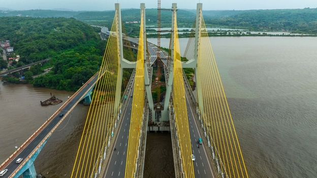 Aerial view of the Zuari Bridge with its distinctive yellow cable stayed design spanning the river surrounded by lush green landscape and nearby roads in Cortalim Goa India.