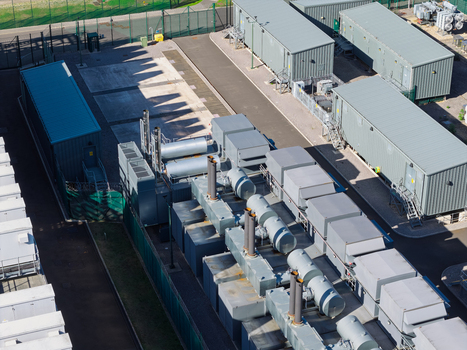 Aerial view of a data center facility featuring industrial cooling units power generators and modular containers within a fenced compound in the United Kingdom.
