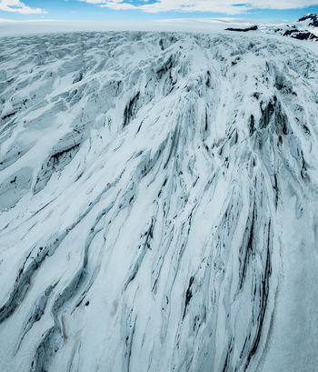 Aerial view of Vatnajokull glacier featuring deep crevasses textured ice formations and snow covered slopes under a clear sky in Iceland.