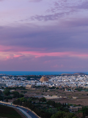 Aerial view of the historic city of Mdina with its prominent dome white stone buildings and surrounding landscape under a vibrant purple sunset sky in Mdina Western Region Malta.