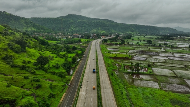 Aerial view of Mumbai Goa Highway cutting through lush green hills and agricultural fields in Mahad Maharashtra India.