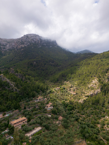 Aerial view of the lush green valley of Valldemossa with stone terraces and traditional houses against the Tramuntana mountains under clouds Valldemossa Balearic Islands Spain.