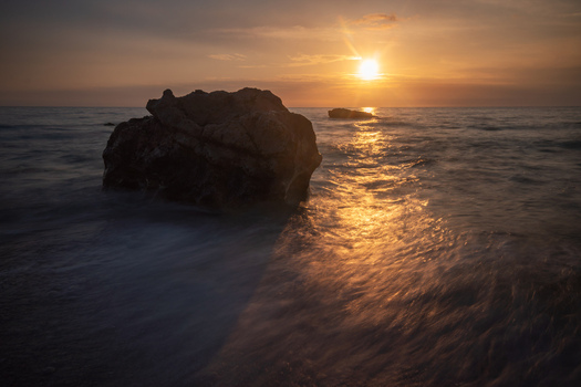 View of golden sunlight kissing the tranquil sea reflecting off the wet sand and rugged rocks at dusk Kathisma Beach Kathisma Lefkada Greece. View of golden sunlight kissing the tranquil sea reflecting off the wet sand and rugged rocks at dusk Kathisma Beach Kathisma Lefkada Greece.