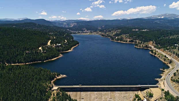 Aerial view of Barker Meadow Reservoir with its dam surrounded by dense pine forests and mountain peaks under a clear blue sky in Boulder County Colorado United States. Aerial view of Barker Meadow Reservoir with its dam surrounded by dense pine forests and mountain peaks under a clear blue sky in Boulder County Colorado United States.