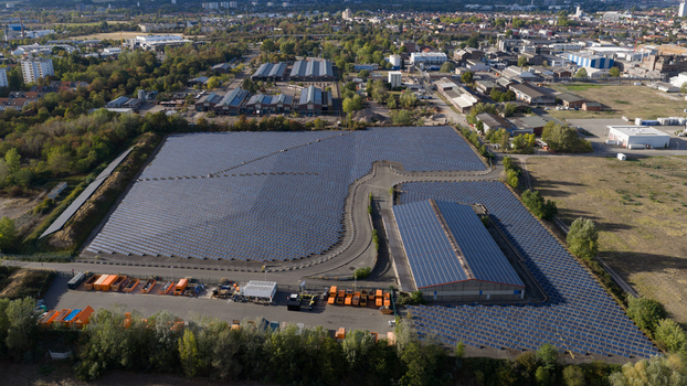 Aerial view of a large solar farm with rows of photovoltaic panels next to an industrial warehouse and surrounding greenery in Ludwigshafen Rhineland Palatinate Germany. Aerial view of a large solar farm with rows of photovoltaic panels next to an industrial warehouse and surrounding greenery in Ludwigshafen Rhineland Palatinate Germany.