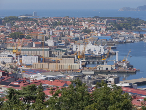 View of the industrial port of Vigo with large cranes cargo ships and urban buildings along the coastline in Vigo Pontevedra Spain.