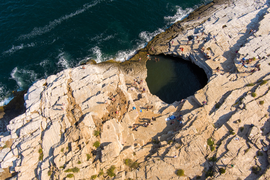 Greece 21 September 2026 Aerial view of Giola Lagoon a natural rock pool in the rocky coastline with people swimming in the clear water and relaxing on the surrounding cliffs. Greece 21 September 2026 Aerial view of Giola Lagoon a natural rock pool in the rocky coastline with people swimming in the clear water and relaxing on the surrounding cliffs.