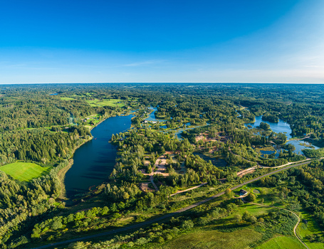 Aerial view of a serene lake surrounded by dense green forests and meadows under a clear blue sky in Latvia. Aerial view of a serene lake surrounded by dense green forests and meadows under a clear blue sky in Latvia.