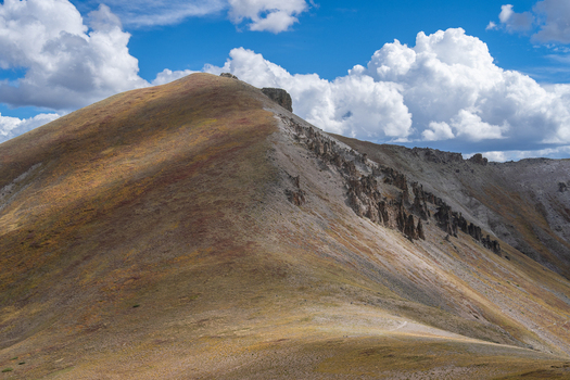 View of the rugged rocky slopes of San Luis Peak under a bright blue sky with dramatic clouds in the alpine landscape of Creede Colorado United States. View of the rugged rocky slopes of San Luis Peak under a bright blue sky with dramatic clouds in the alpine landscape of Creede Colorado United States.