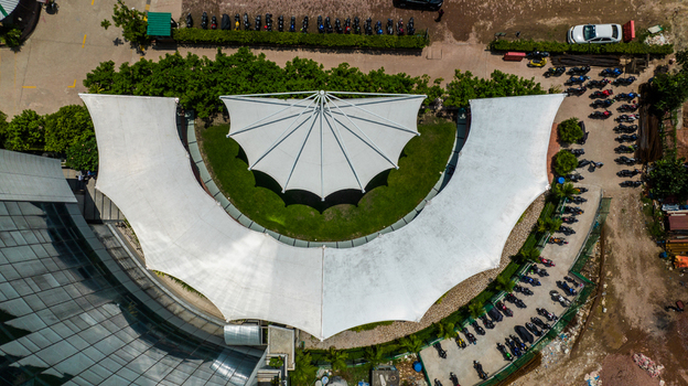 Aerial view of a white tensile canopy structure covering a green lawn with a modern building and a parking area filled with motorcycles in Dhaka Dhaka Division Bangladesh. Aerial view of a white tensile canopy structure covering a green lawn with a modern building and a parking area filled with motorcycles in Dhaka Dhaka Division Bangladesh.