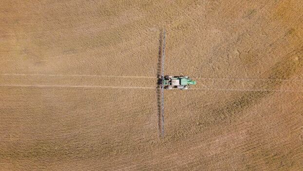 Aerial view of a tractor spraying a vast agricultural field with golden crops showing tire tracks and patterns in the soil in Philadelphia Western Cape South Africa. Aerial view of a tractor spraying a vast agricultural field with golden crops showing tire tracks and patterns in the soil in Philadelphia Western Cape South Africa.