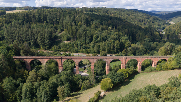 Aerial view of the historic red sandstone Himbaechel Viaduct spanning a lush green valley with dense forests and rolling hills in Erbach Hessen Germany.