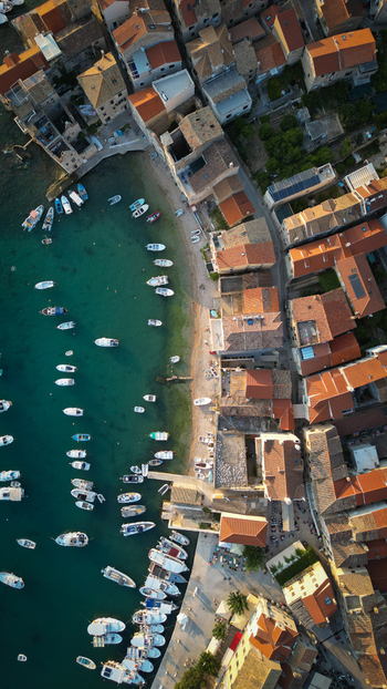 Aerial view of Komiza harbor with numerous boats moored in turquoise water next to historic stone buildings and red tiled rooftops Komiza Split Dalmatia County Croatia.