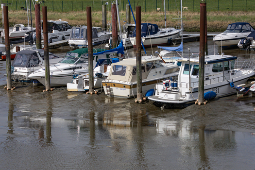 View of motorboats and yachts moored at the Dangast harbor during low tide with tall pilings and green meadows in the background Varel Lower Saxony Germany. View of motorboats and yachts moored at the Dangast harbor during low tide with tall pilings and green meadows in the background Varel Lower Saxony Germany.