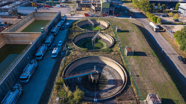 Aerial view of the sewage works in Camberley showing circular sedimentation tanks industrial infrastructure and a line of tanker trucks parked nearby in Camberley England United Kingdom.