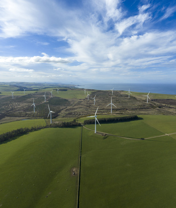 Aerial view of wind turbines on rolling green hills overlooking the sea under a blue sky in Scotland United Kingdom. Aerial view of wind turbines on rolling green hills overlooking the sea under a blue sky in Scotland United Kingdom.