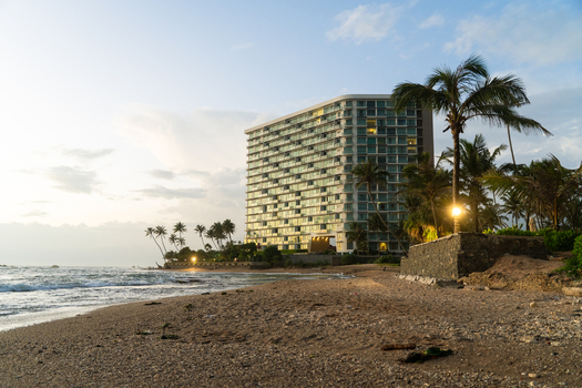 View of a modern high rise hotel building on a sandy beach with palm trees and ocean waves at sunset in Galle Southern Province Sri Lanka.