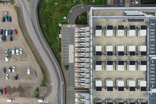 Aerial view of a data center rooftop featuring rows of industrial cooling units and ventilation systems next to a parking lot in United Kingdom.