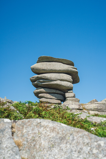View of the Cheesewring rock formation a natural granite tor with stacked stones set against a clear blue sky in the moorland landscape of Minions Cornwall United Kingdom. View of the Cheesewring rock formation a natural granite tor with stacked stones set against a clear blue sky in the moorland landscape of Minions Cornwall United Kingdom.